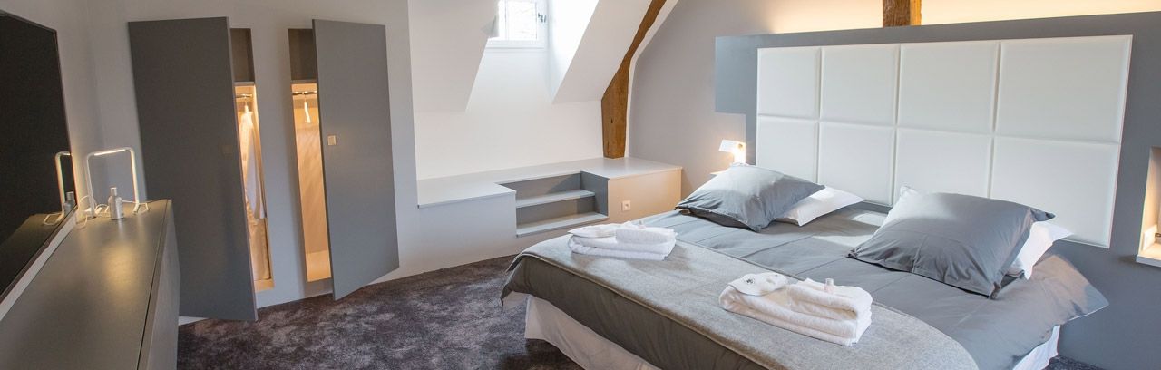 Chambre à coucher d'une des Suites de Cheverny : placards, grand lit double avec tête de lit, peignoirs et serviettes sur le lit.